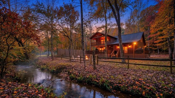 A cabin with a deck, surrounded by trees and a stream. - Private Cozy Cabin w/ Hot Tub in Blue Ridge! (Blue Ridge)