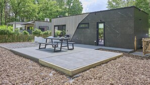 A modern building with a flat roof, a patio area with a table and benches, and a wooden fence.