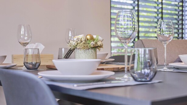 A dining table set with plates, bowls, and wine glasses, with a decorative vase in the center.