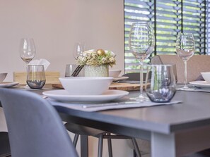 Une table à manger dressée avec des assiettes, des bols et des verres à vin, et un vase décoratif placé au centre.