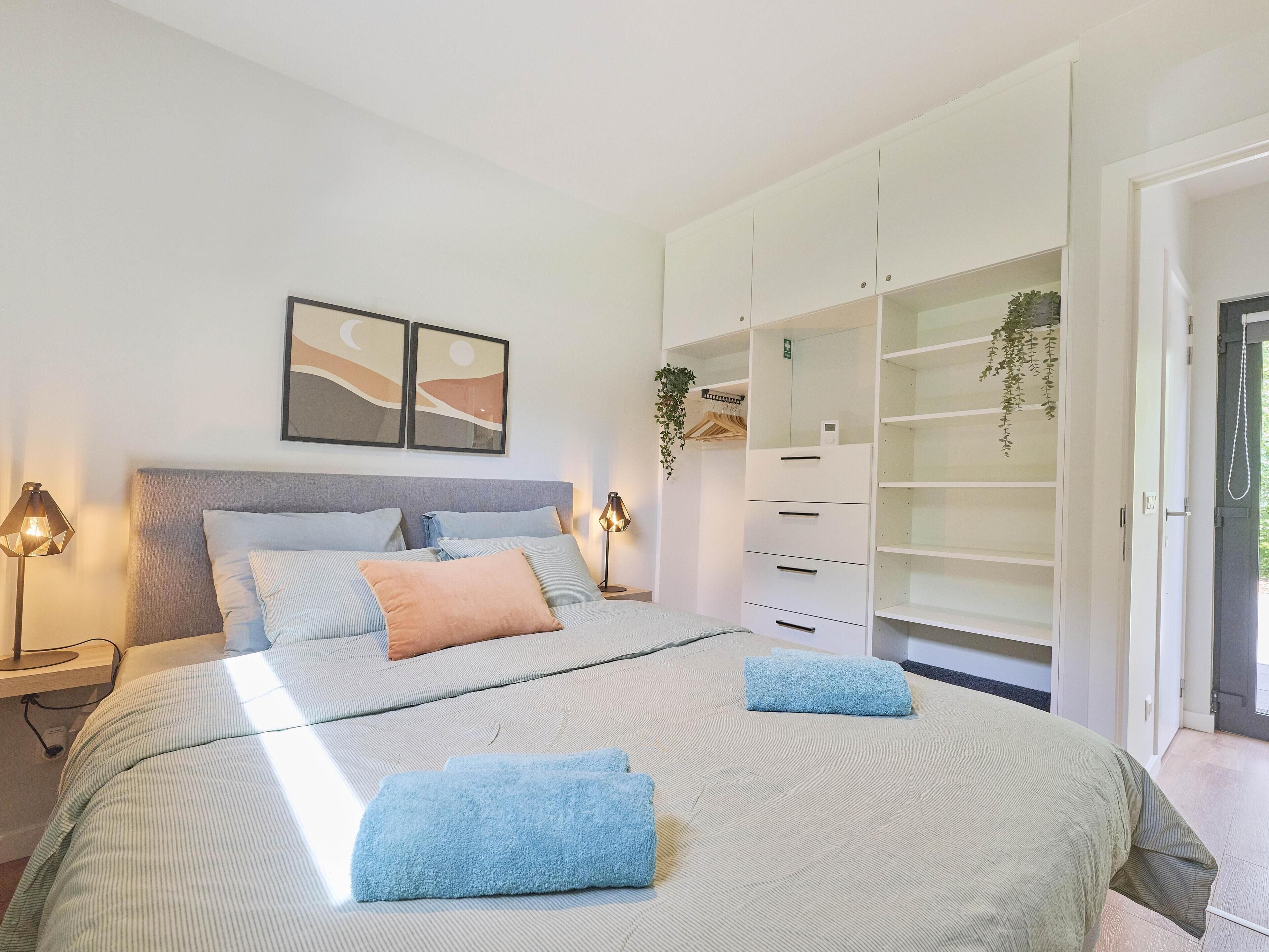 A bedroom with a bed, bedside lamps, a wardrobe, and a door leading to another room.