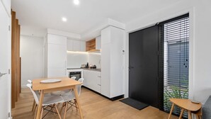 A modern kitchen with white cabinets, a wooden dining table, and a black door.