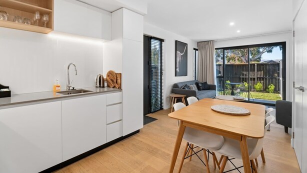 A modern kitchen with white cabinets, a wooden countertop, and a dining area with a wooden table and chairs.