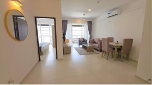 Una habitación de hotel moderna con una cama, una zona de estar con sofá y sillones, una mesa de comedor y un espejo grande.