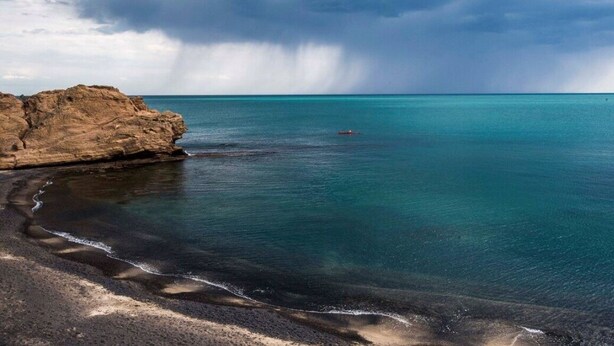 A coastal landscape with a rocky shoreline, calm turquoise waters, and a distant view of a stormy sky. - Maison Basalte studio 1 (Agde)
