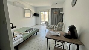 A compact hotel room with a bed, a desk with a coffee maker, a chair, and a TV on the wall. - Maison Basalte studio 1 (Agde)