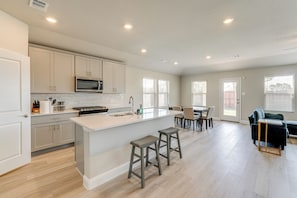 A modern kitchen with white cabinets, a large island with stools, a microwave, and a dining area with a table and chairs.