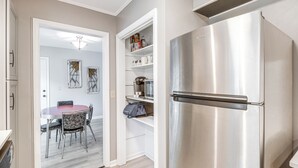 Una cucina moderna con un frigorifero in acciaio inossidabile, un'area pranzo con un tavolo rotondo e sedie, e una dispensa con scaffali.
