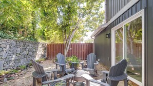 Una veranda esterna con poltrone Adirondack e un tavolo, circondata da un muro in pietra e una recinzione in legno.
