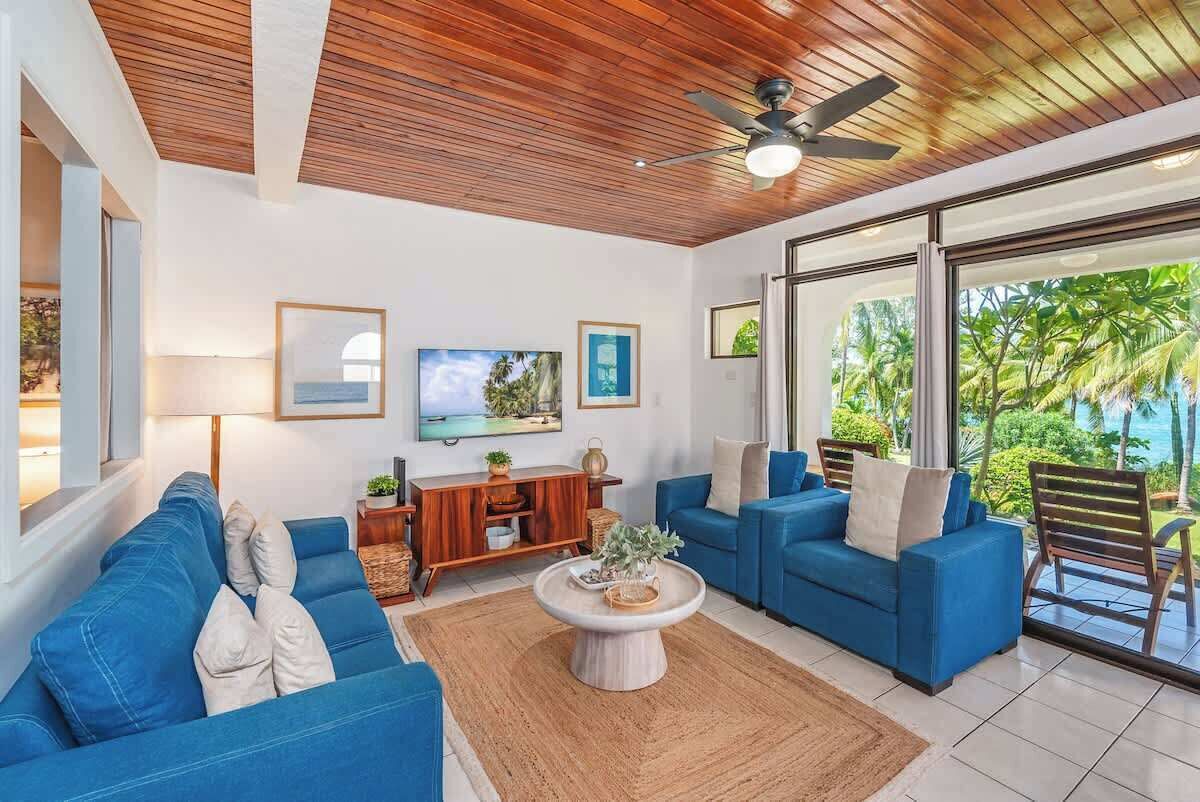 A modern living room with a wooden ceiling, two blue sofas, a coffee table, and a TV on the wall.