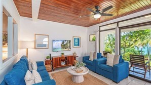 Una sala de estar moderna con techo de madera, dos sofás azules, una mesa de centro y un televisor en la pared.