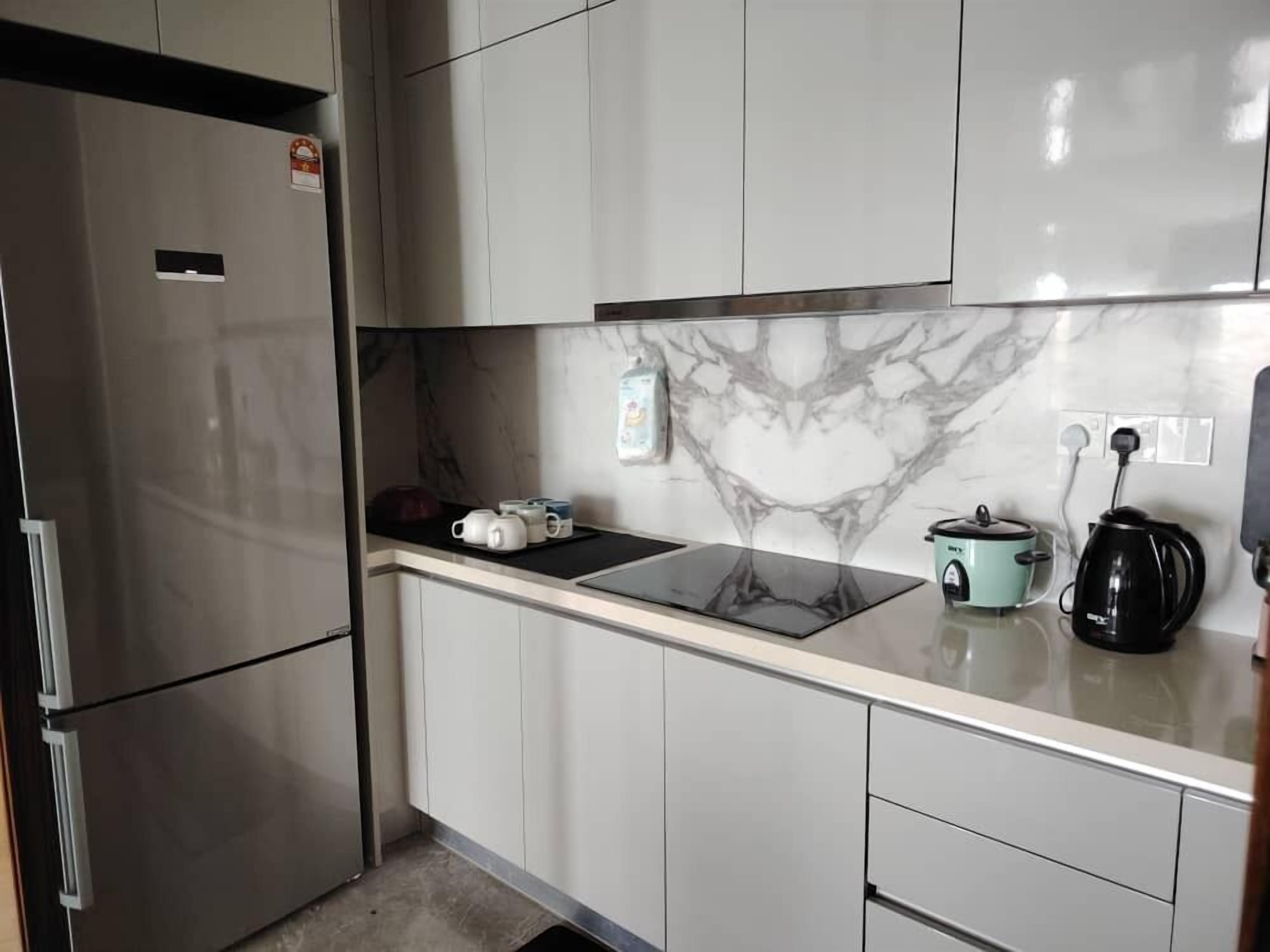 Una cocina moderna con refrigerador empotrado, cocina por inducción negra y una olla de cocción lenta color verde azulado.