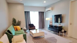 A modern living room with a green sofa, a white armchair, a coffee table, and a TV mounted on the wall. - Platinum 2 KLCC By Natol Chain Of Homestays (Kuala Lumpur)