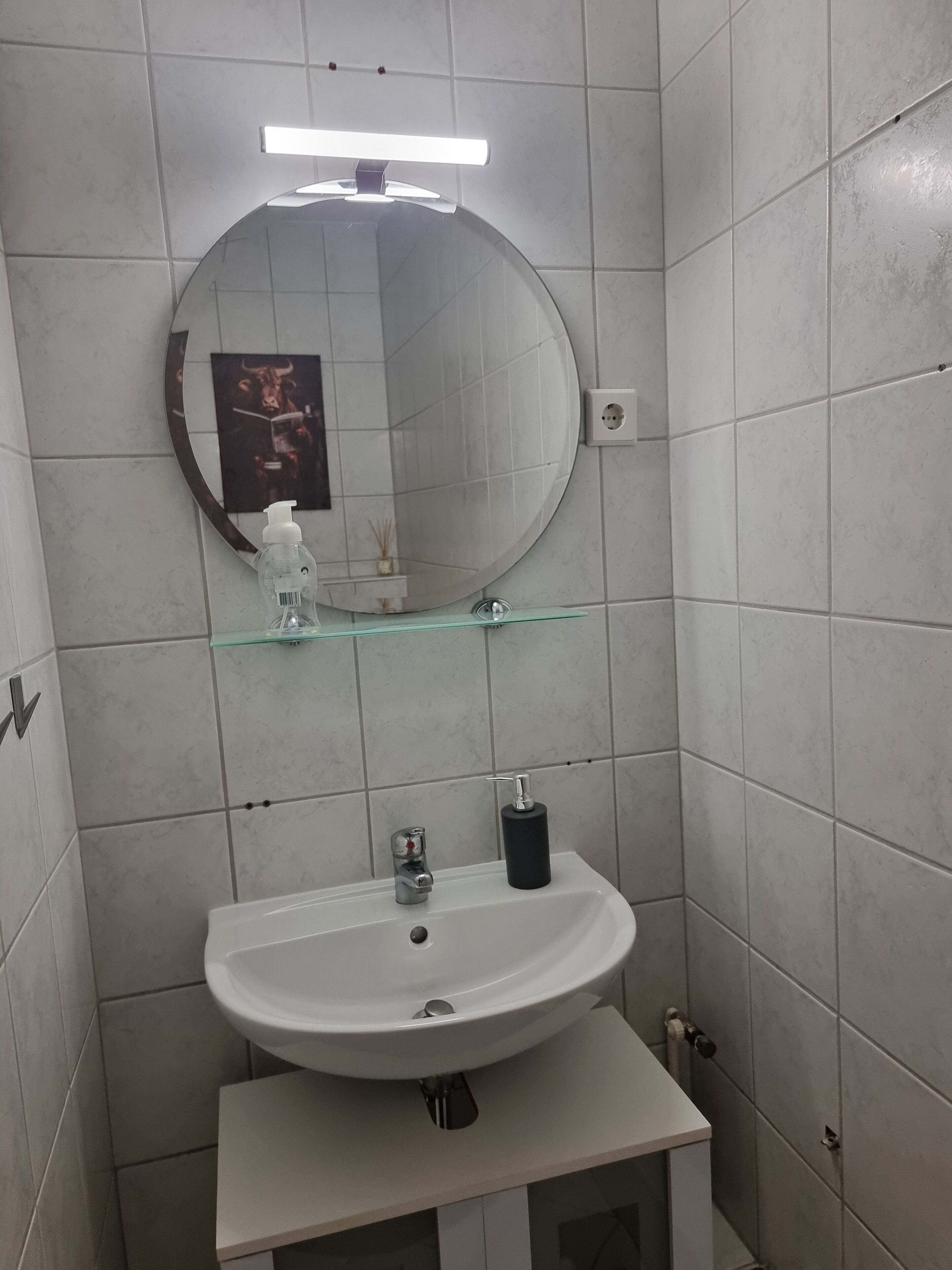 A bathroom with a white sink, a round mirror, and a glass shelf.