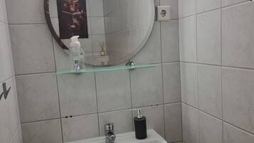 A bathroom with a white sink, a round mirror, and a glass shelf.