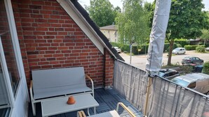 Ein Balkon mit Tisch und Stühlen, eine Ziegelwand und Blick auf parkende Autos und Bäume.