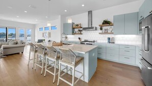 A modern kitchen with a central island, bar stools, and a view to the outside. - Tranquil Tides-Luxury Waterfront home, pool & dock (Kingsland)