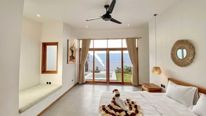 Un dormitorio amplio con una cama grande, un ventilador de techo, vista al mar y un balcón.