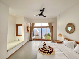 A spacious bedroom with a large bed, a ceiling fan, a view of the sea, and a balcony.
