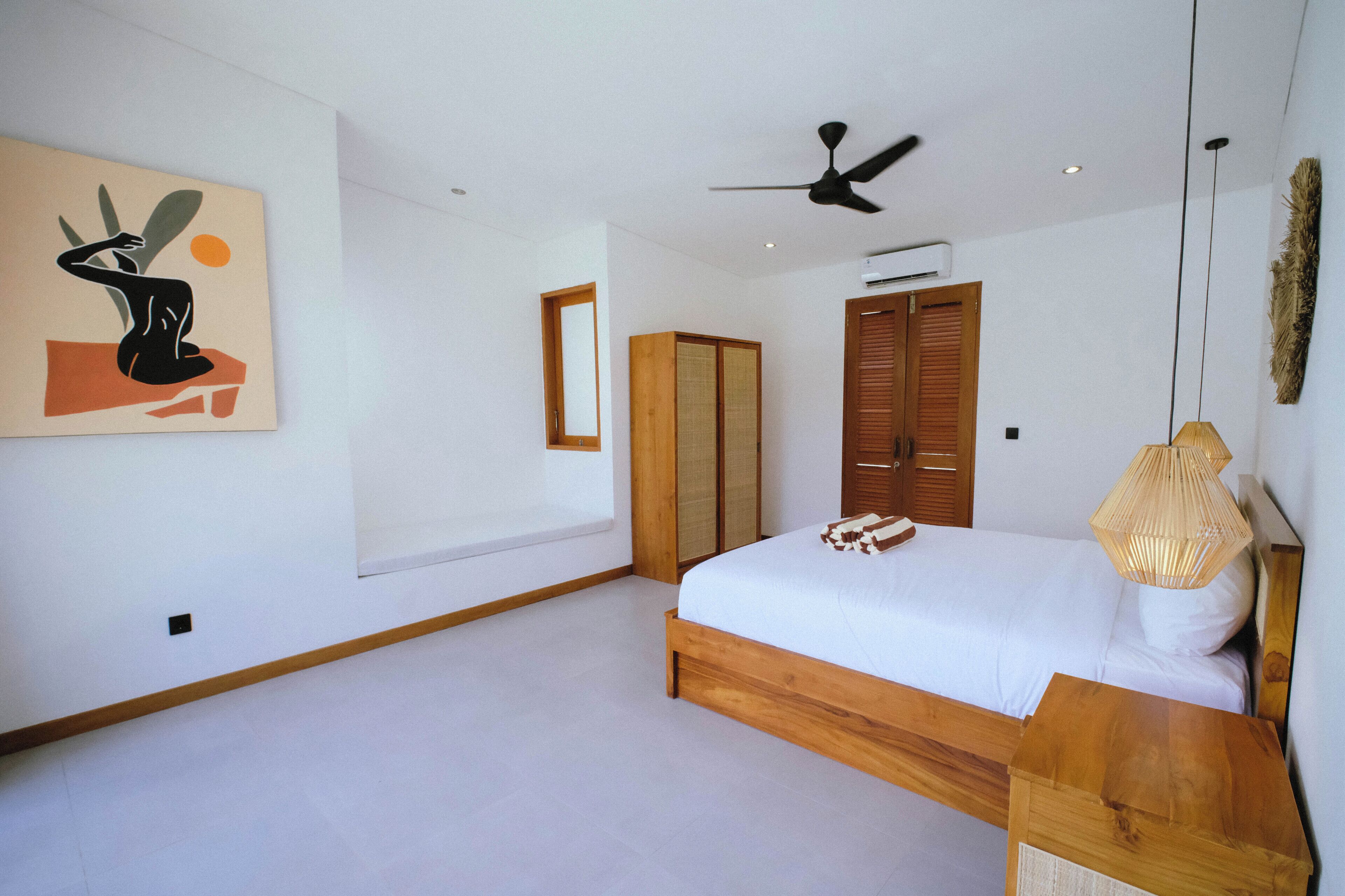 Un dormitorio moderno con una cama grande, cabecera de madera, ventilador de techo y una obra de arte colgada en la pared.