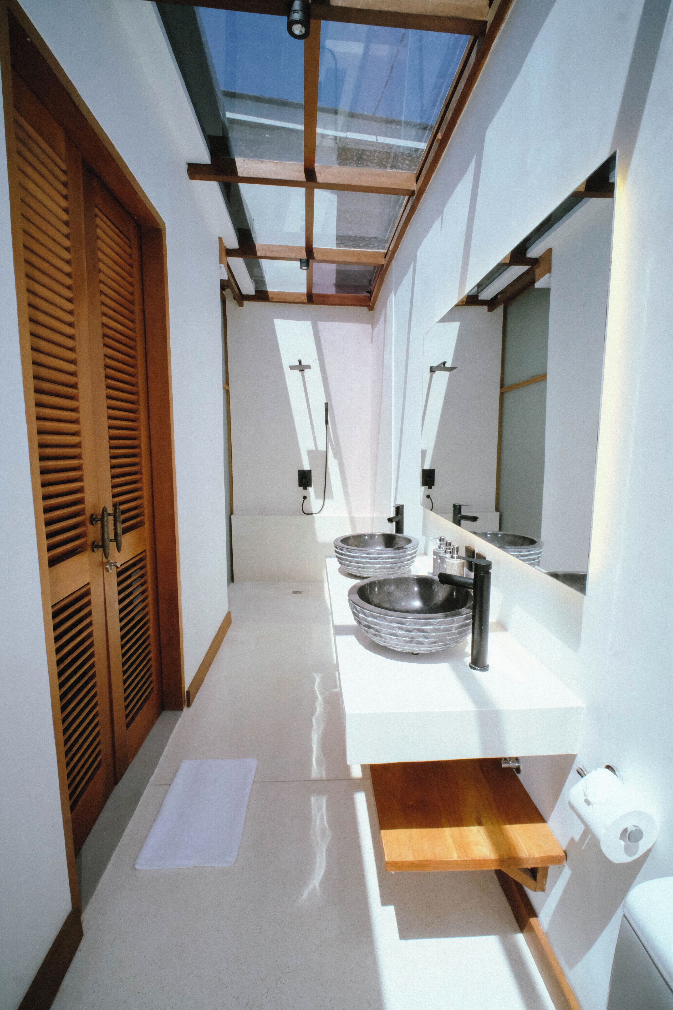 A narrow bathroom with a skylight, wooden door, and two sinks.