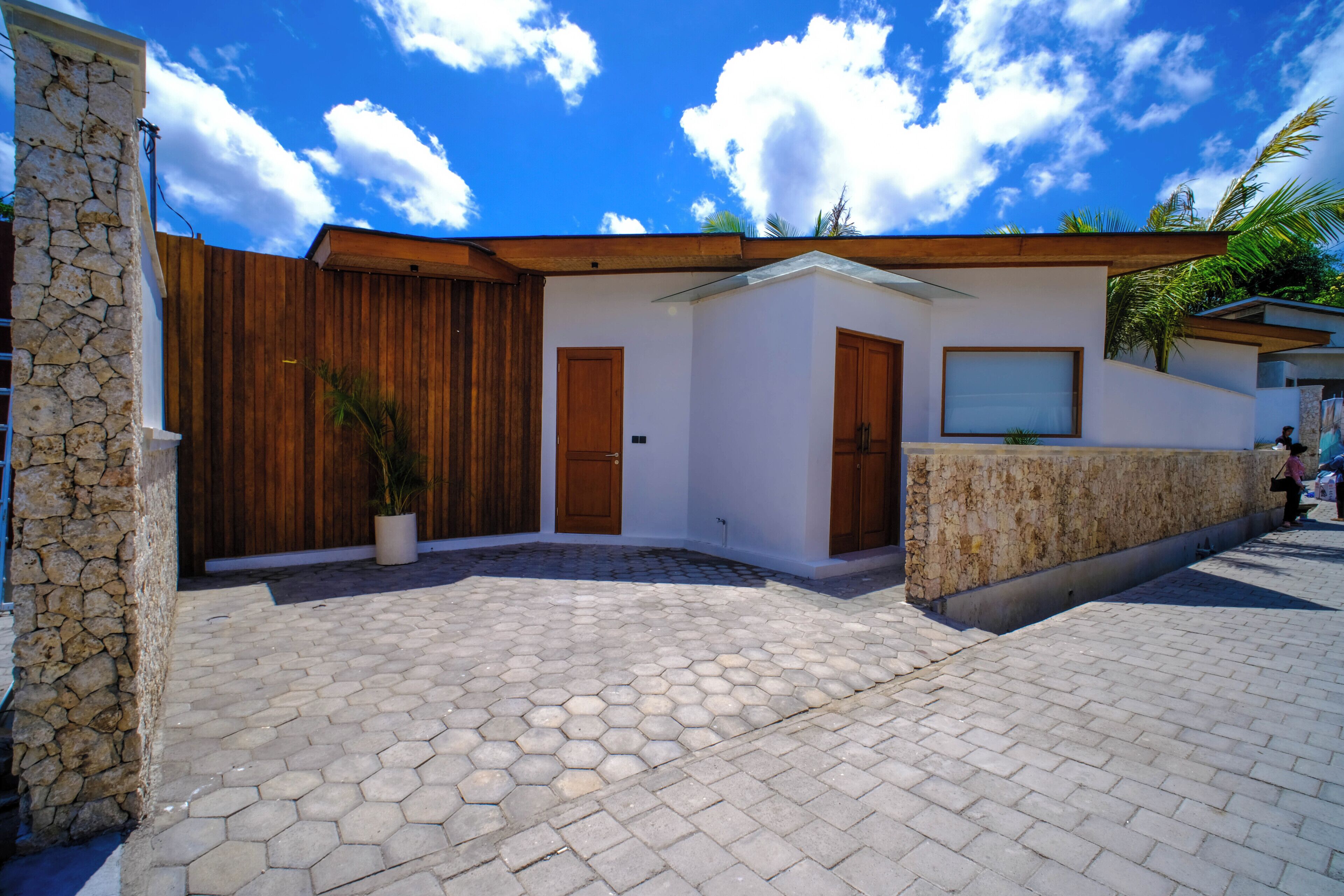 Una casa moderna con un muro de piedra, valla de madera y un patio empedrado.