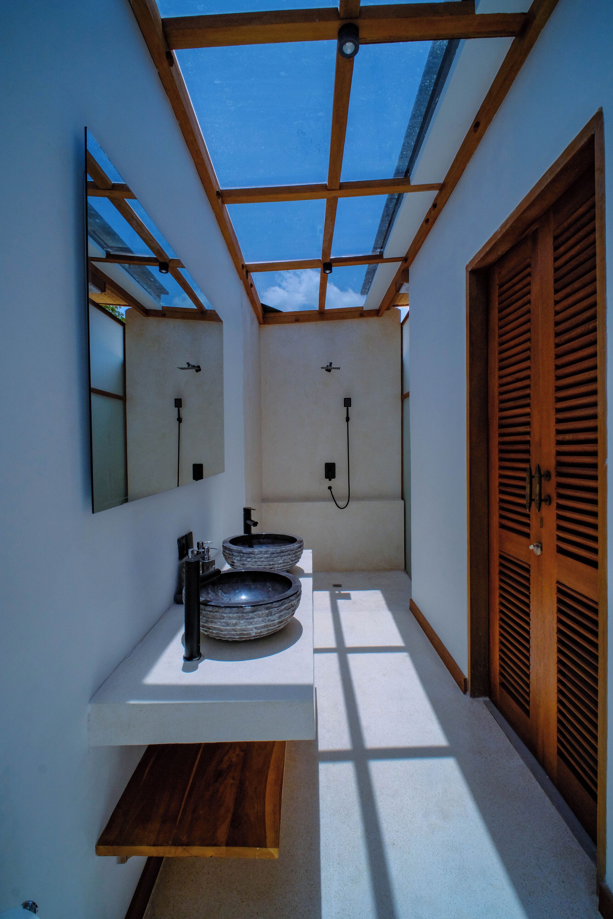 A modern bathroom with a skylight, wooden beams, a large mirror, and a wooden door.