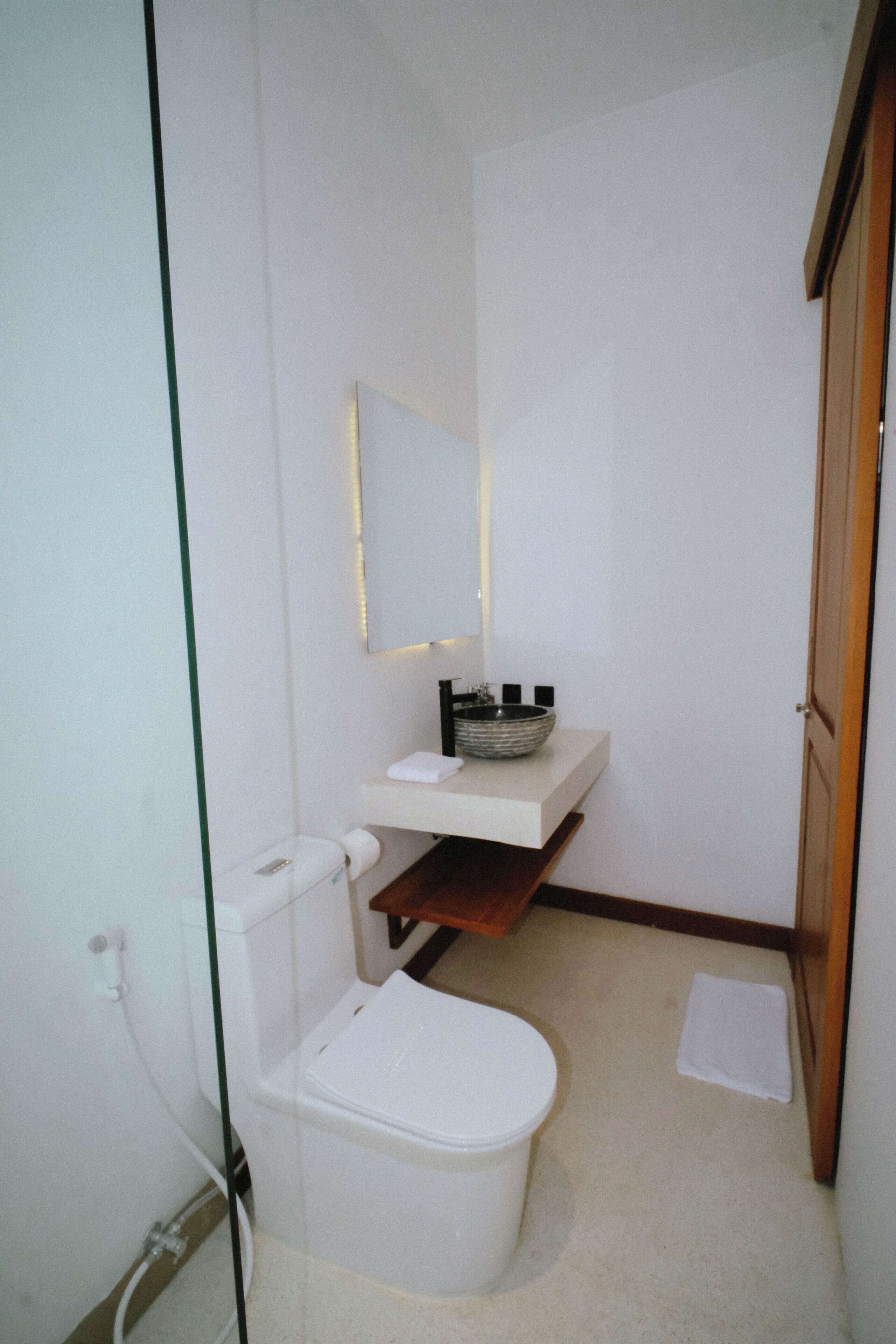 A compact bathroom with a toilet, a sink with a mirror above, and a small shelf.