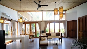 A spacious living area with a ceiling fan, large windows, and a dining area with a table and chairs. - Maravilla Complex (Penida Island)