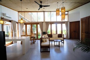 A spacious living area with a ceiling fan, large windows, and a dining area with a table and chairs.