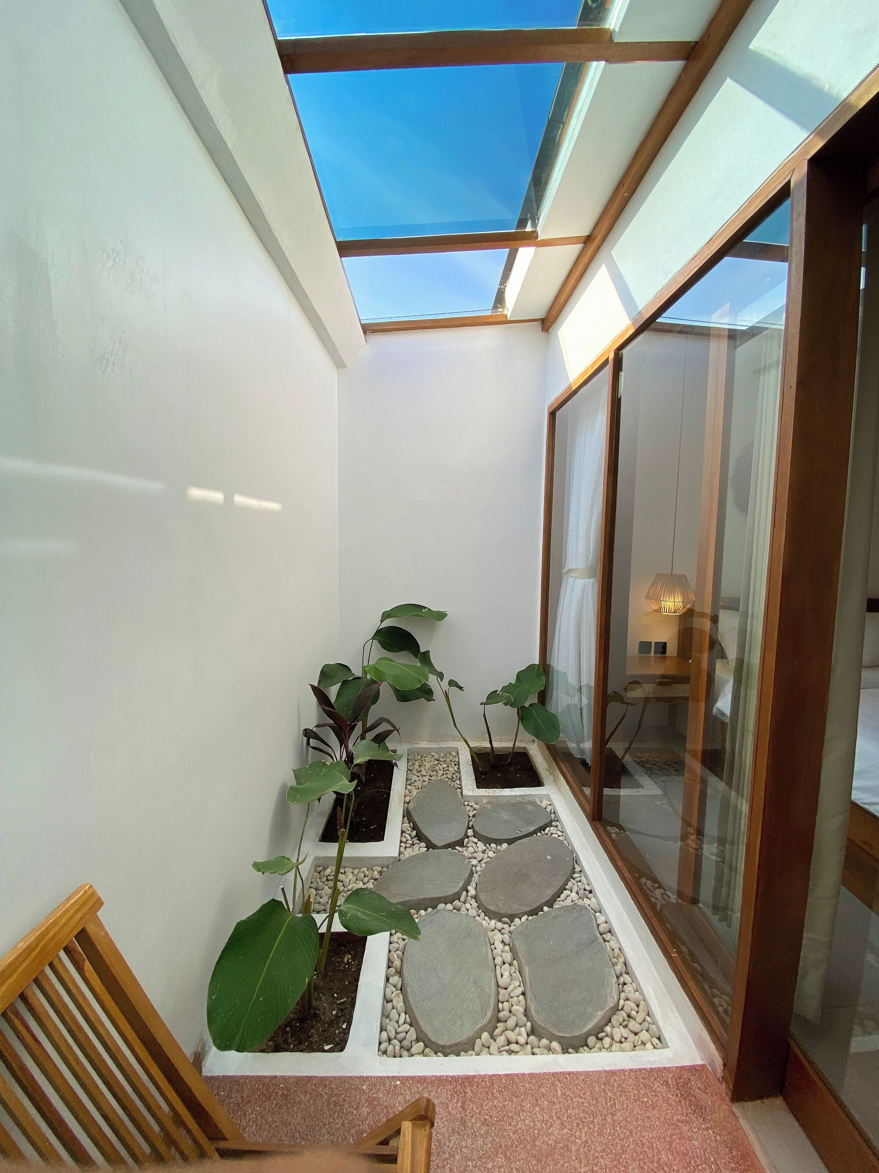 Un corridoio stretto con una luce sul soffitto, piante in vaso e un sentiero in pietra che conduce a una stanza con un letto e una lampada.
