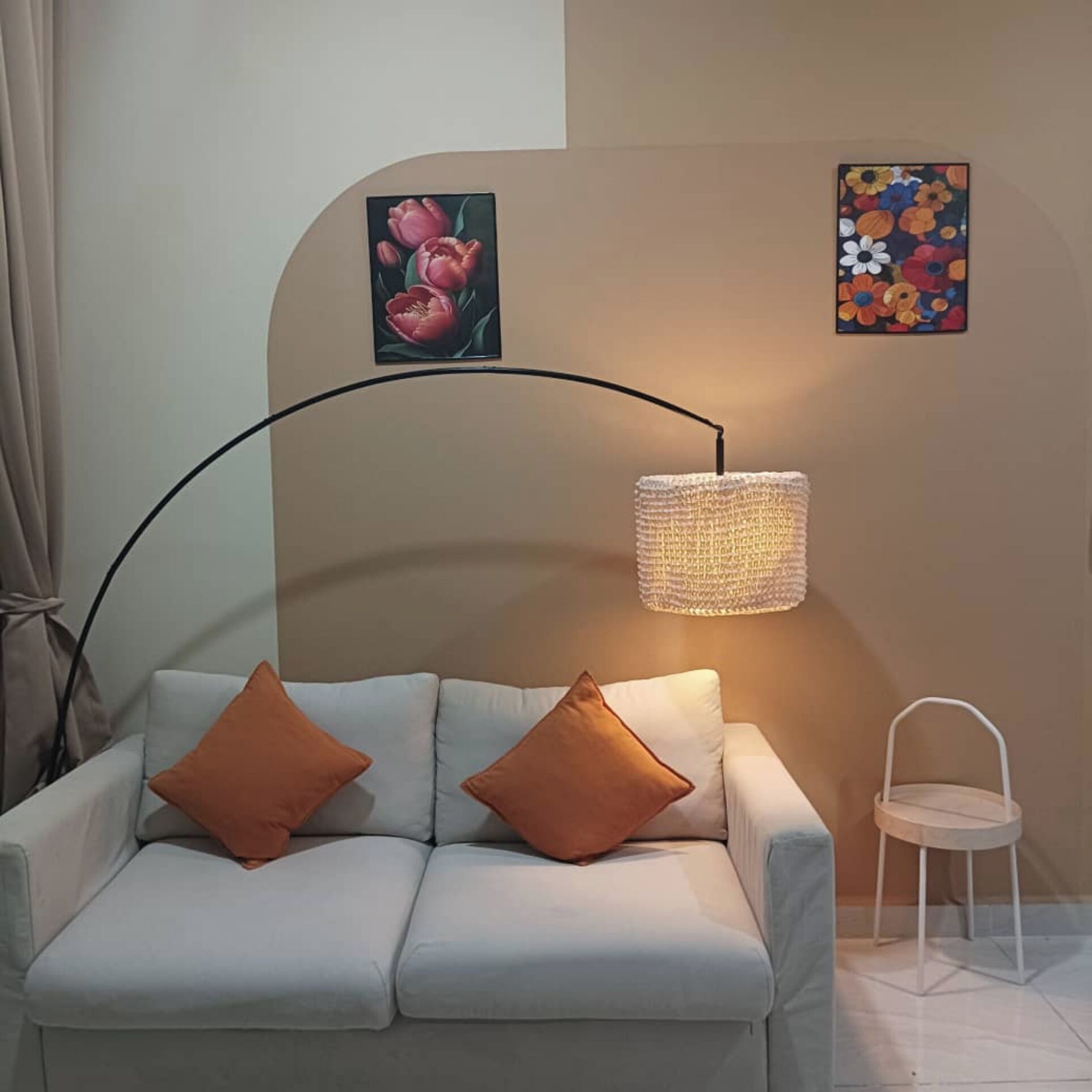 A modern living room with a white sofa, two orange cushions, a floor lamp, and two wall art pieces.