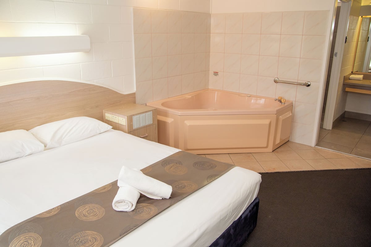 Quarto de hotel com uma cama grande, uma banheira e uma mesa de cabeceira.