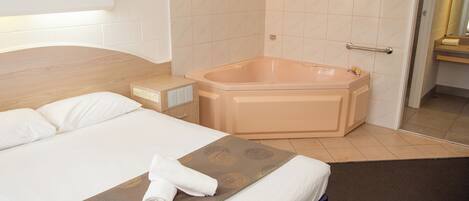 A hotel room with a large bed, a bathtub, and a bedside table.