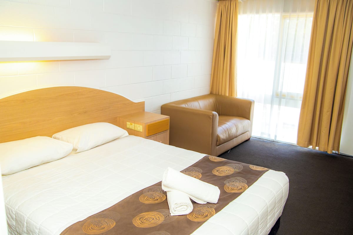 Quarto de hotel com cama, uma cadeira, mesa de cabeceira e janela com cortinas.