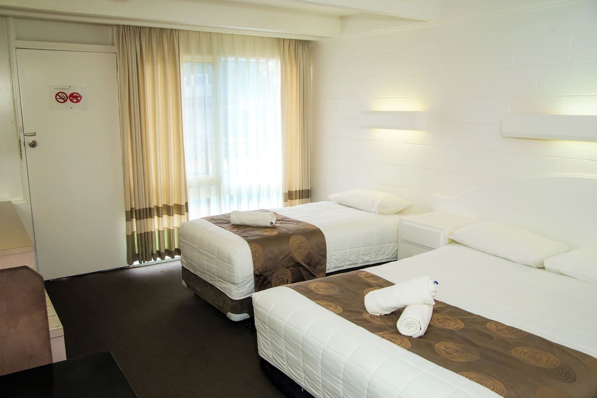 Quarto de hotel com duas camas, uma secretária e uma porta com o aviso 'não fumar'.