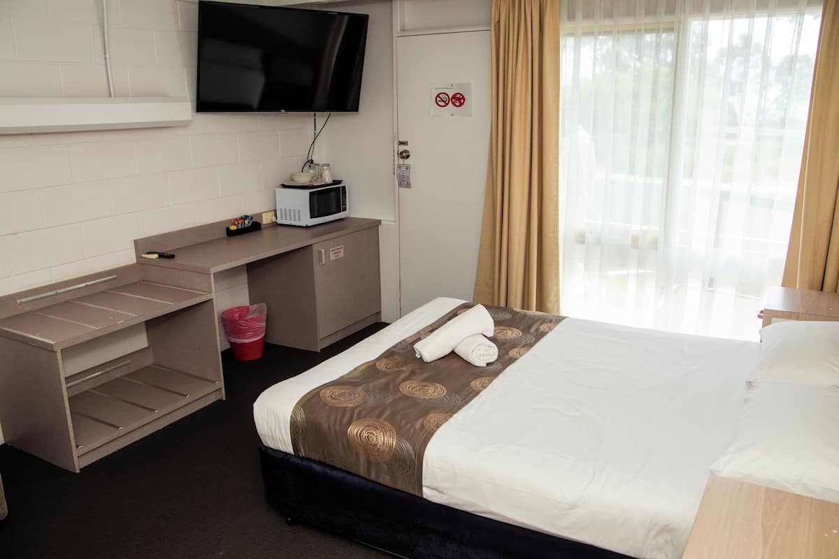 Quarto de hotel com cama, secretária com micro-ondas, televisão e janela com cortinas.