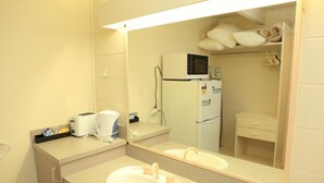 A hotel bathroom with a sink, mirror, microwave, and a small refrigerator. - Ocean Views Motel Lakes Entrance (Kalimna)