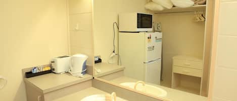 Ein Hotelbad mit Waschbecken, Spiegel, Mikrowelle und kleinem Kühlschrank.