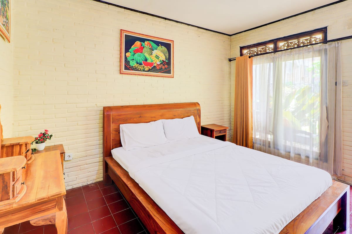 Una cama bien hecha con sábanas blancas en una habitación con pared de ladrillo, cabecera de madera y mesita de noche de madera con una lámpara.