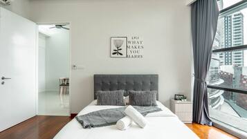 A modern bedroom with a large bed, grey headboard, and a city view.