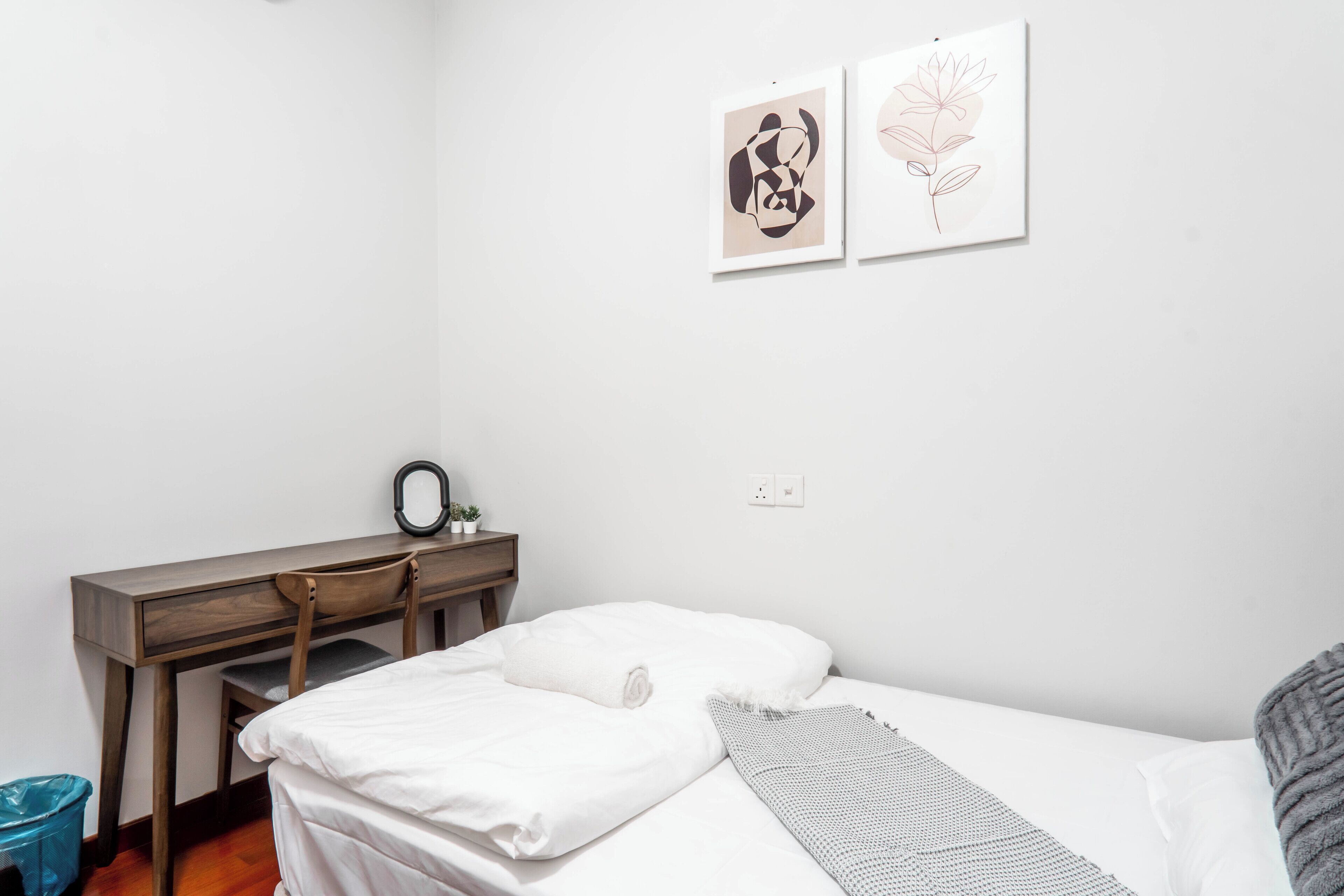 A bedroom with a bed, a desk, and two framed artworks on the wall.