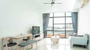Una sala moderna con comedor, un sofá, un televisor y ventanas grandes con cortinas.