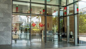 Una entrada de hotel moderna con puertas de vidrio, un mostrador de recepción y faroles decorativos rojos.