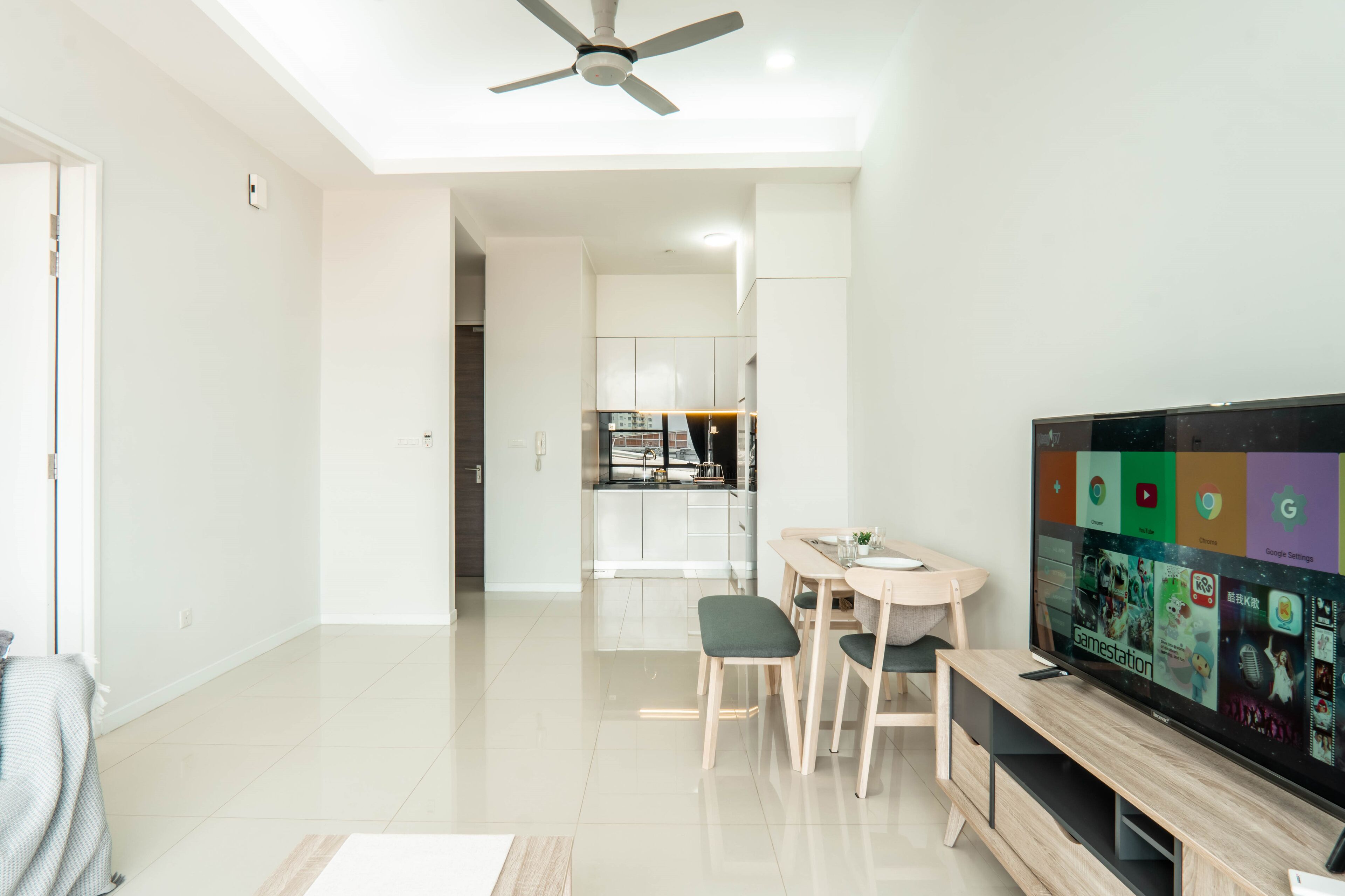 A modern living room with a flat-screen TV, a ceiling fan, and a dining area with a kitchen in the background.