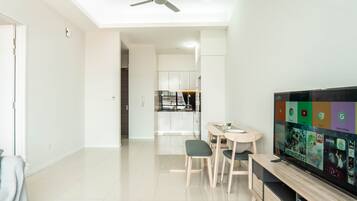 A modern living room with a flat-screen TV, a ceiling fan, and a dining area with a kitchen in the background.