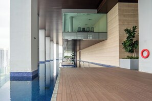 A modern indoor swimming pool area with a wooden deck, glass walls, and a seating area with chairs. - Azure Residences Kelana Jaya by Airhost (Petaling Jaya)