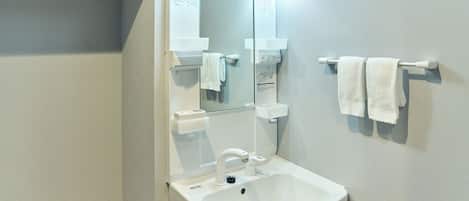 Un baño con lavamanos blanco, espejo y toallero.