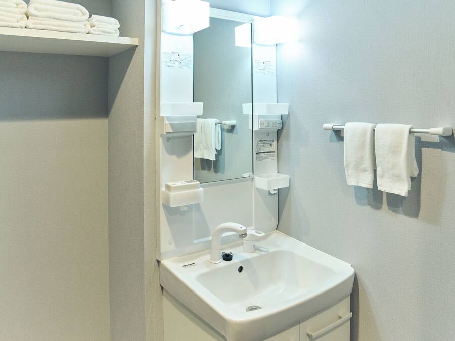 Un baño con lavamanos blanco, espejo y toallero.