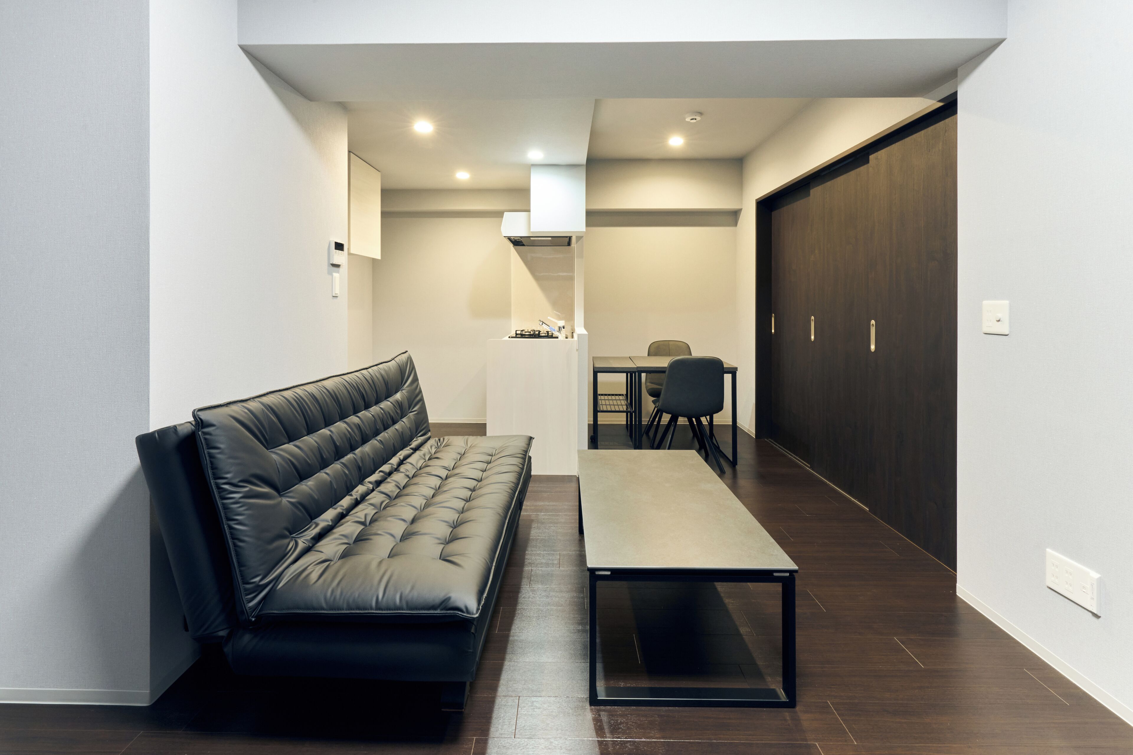 A modern living room with a black leather sofa, a small table, and a dining area with a table and chairs.